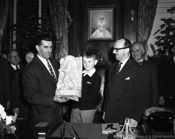 Pierre Drapeau remettant un cadeau au hockeyeur Maurice Richard à l'occasion de son 400e but dans la Ligue nationale de hockey (LNH), en présence de son père, le maire Jean Drapeau, et du journaliste Charles Mayer, 21 décembre 1954, VM94-Z558-2