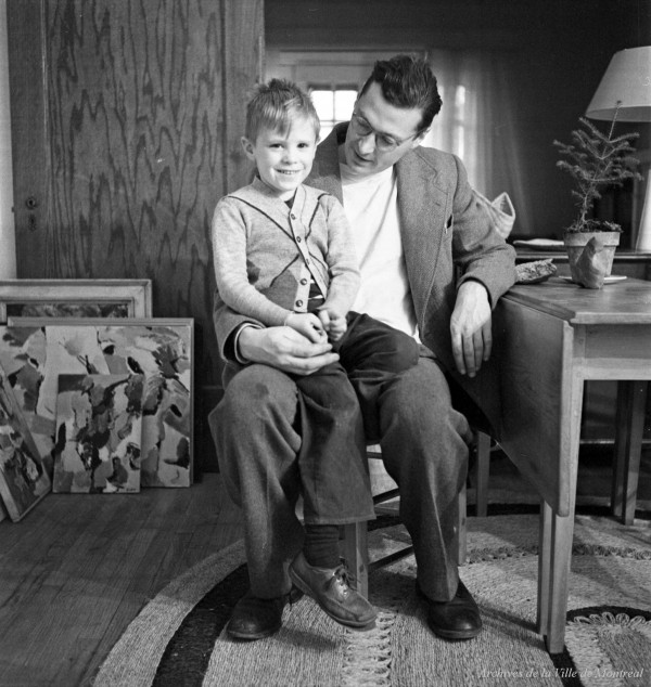 Le peintre Paterson Ewen assis avec son fils chez lui. Des tableaux se trouvent dans le coin.  – Novembre 1955. Photographie de Robert Millet. P179-Y-01-02-D004-P268. AVM.